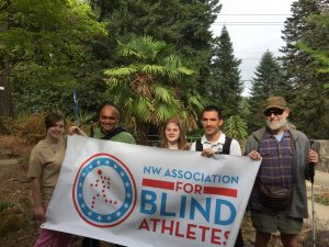Prateek and fellow program participants smile and hold up NWABA banner with many trees in the background