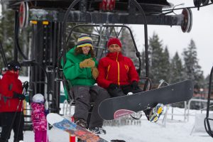 Prateek and a volunteer smiling on a ski lift with snowboards