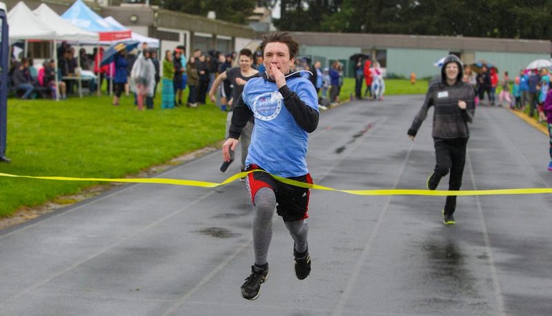 Young man crossing a finish line with yellow tape across.