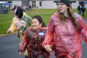 Guide and young girl running hand in hand wearing rain ponchos.