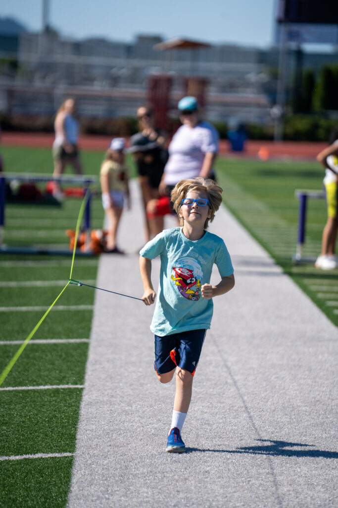 Young boy with glasses holding on to a tether running forward.