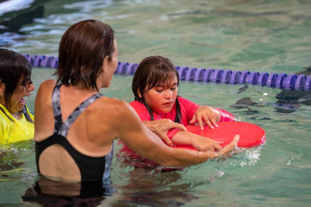 A counselor is teaching a young girl how to use a kickboard in the pool.