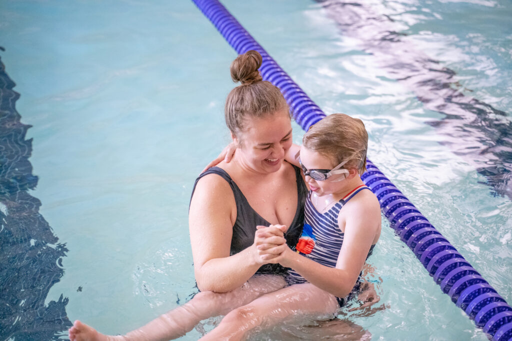 Female volunteer holding a young girl wearing goggles in the pool.