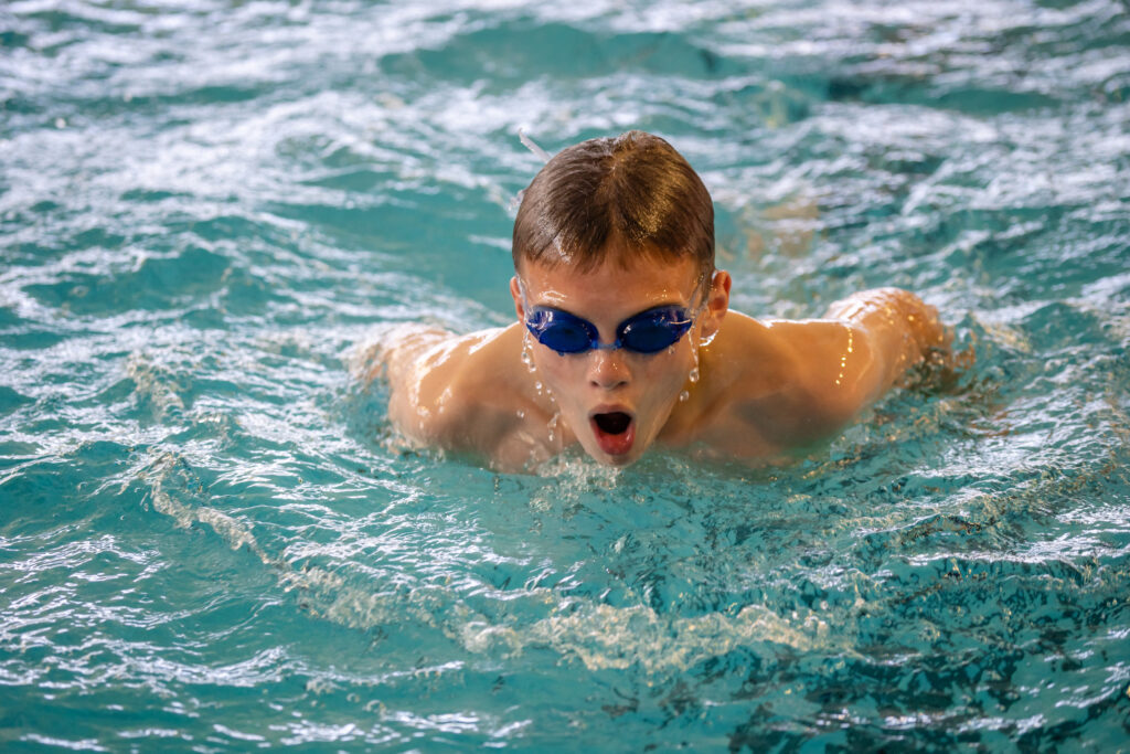 Young boy wearing goggles swimming the breast stroke.