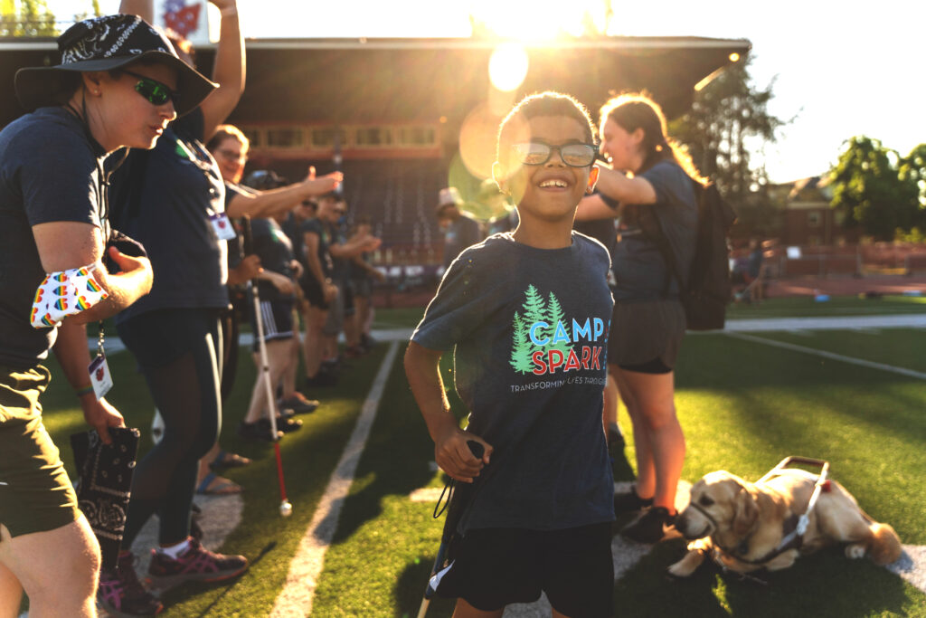 Young boy with a Camp Spark tshirt running past a cheering line of counselors.