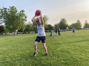 Female athlete standing in a grassy field holding a ball over her head getting ready to throw it.