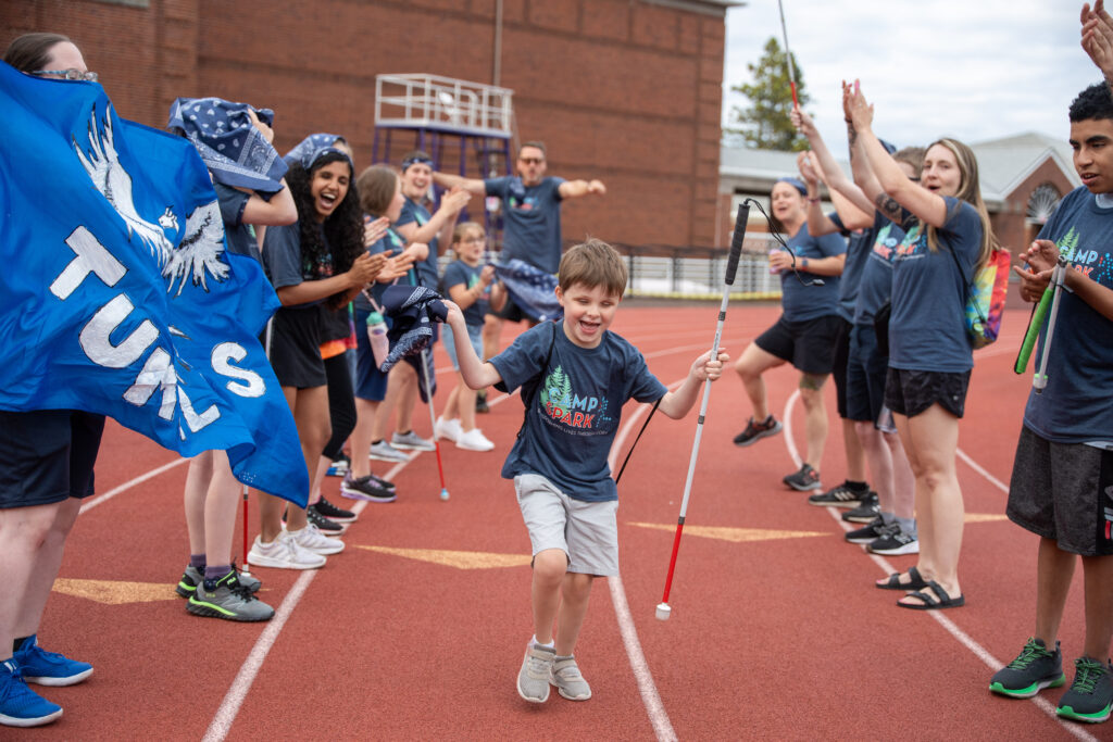 Young athlete walking past a cheering crowd of counselors holding his cane with a big smile on his face.