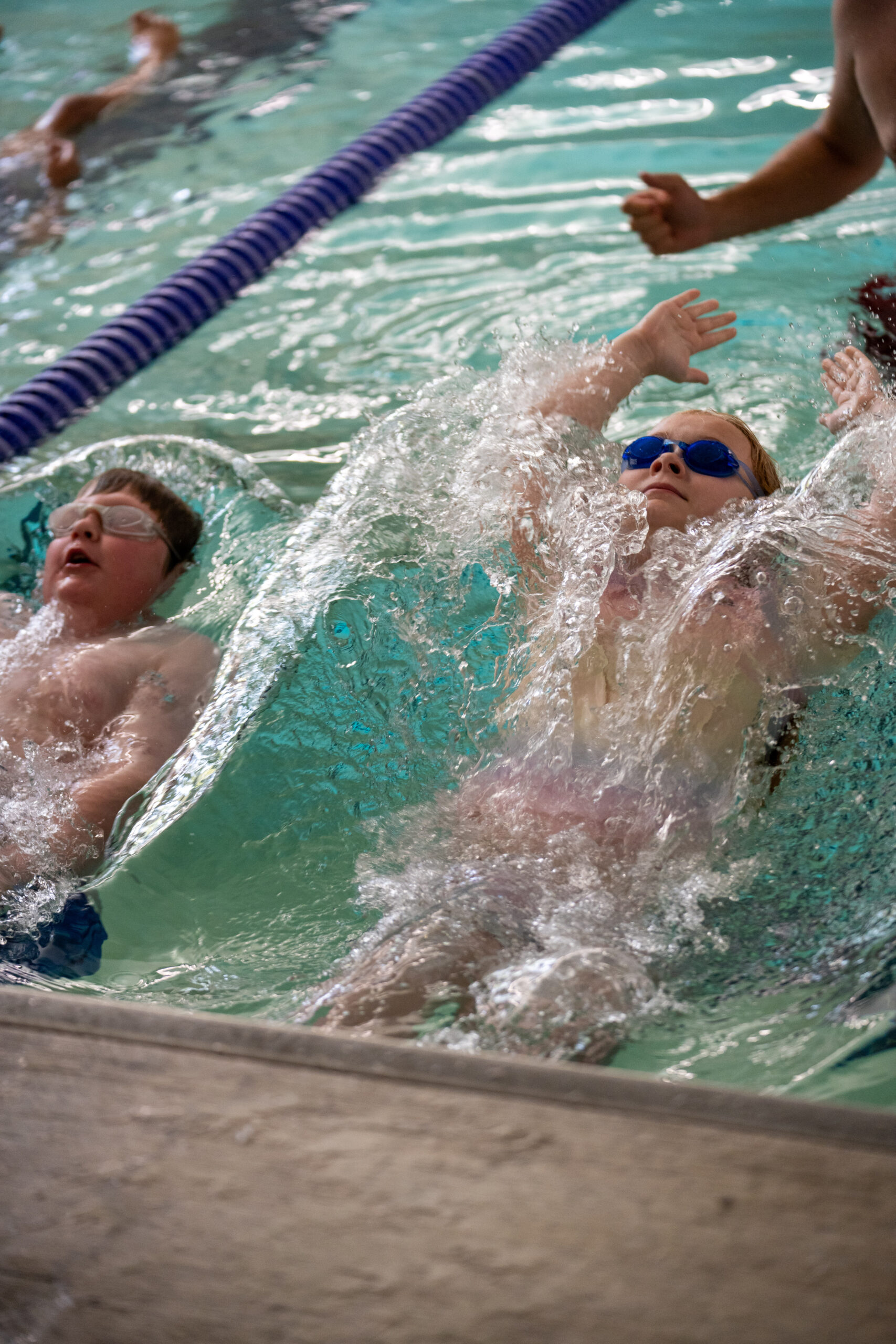 Two young athletes in a pool pushing off the wall into a backstroke.