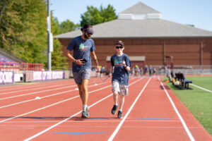 Athlete Kaleb R. runs alongside a Camp Spark counselor on a track connected by a tether.