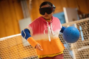 Camper, Inara, holding a blue goalball behind her posing to throw the ball forward.
