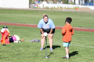 stacey looks on as an athlete begins to swing a beep basball from a tee