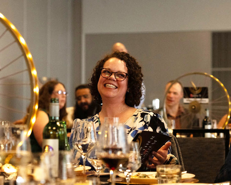 A person smiling at their dinner table during the appeal portion of the event