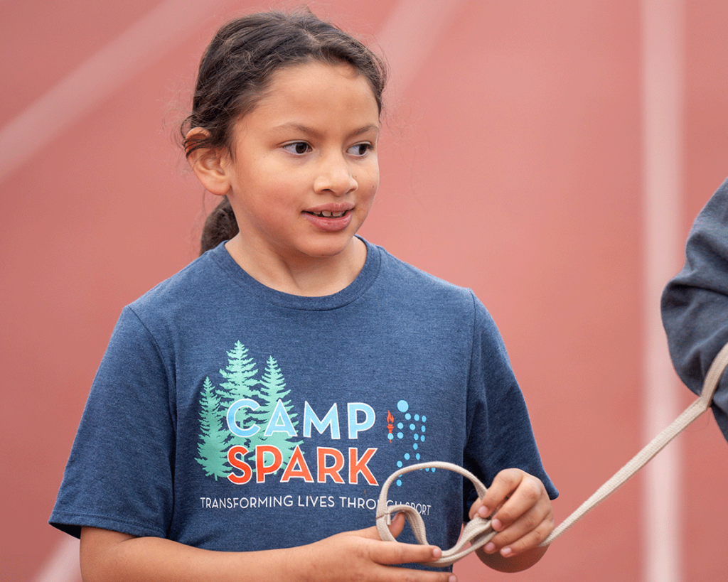 Child athlete, Tianna, on a track in a Camp Spark shirt, holding a tether