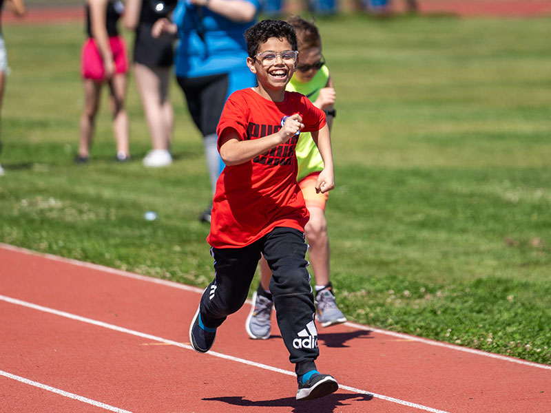 young boy running on a track with a big smile on his face