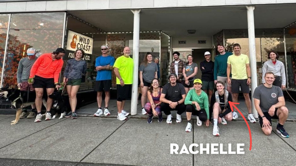 A group of runners in front of a storefront, smiling for a group photo. Rachelle is kneeling in the front of the group.