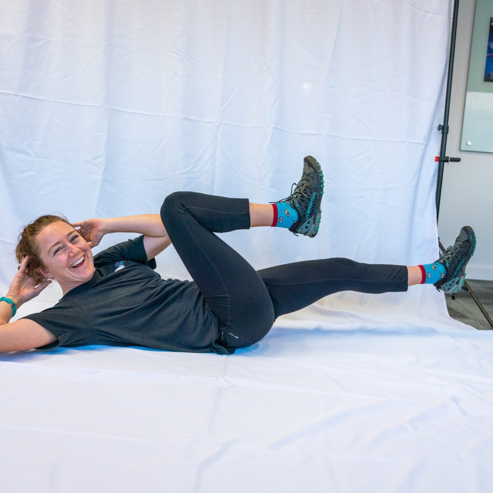 Female staff member demonstrating a crunch on a white backdrop.