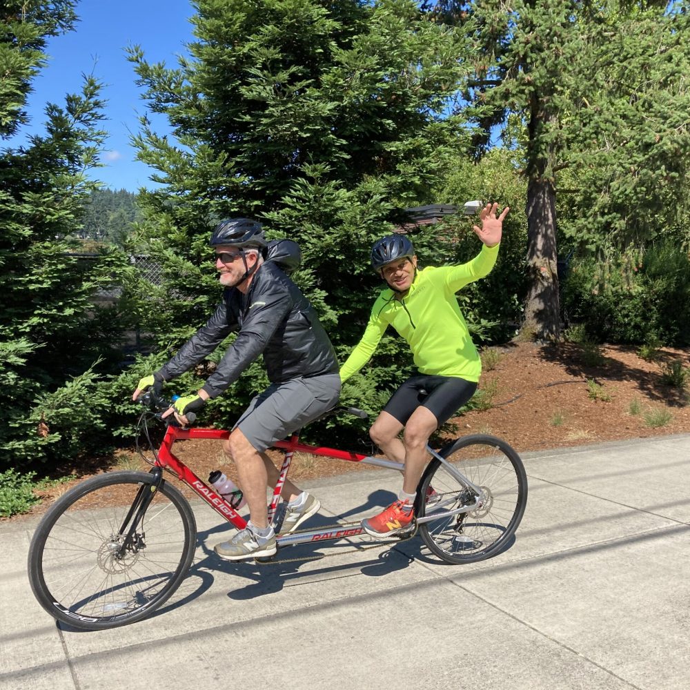 Athlete and guide riding tandem with the athlete waving at the camera.